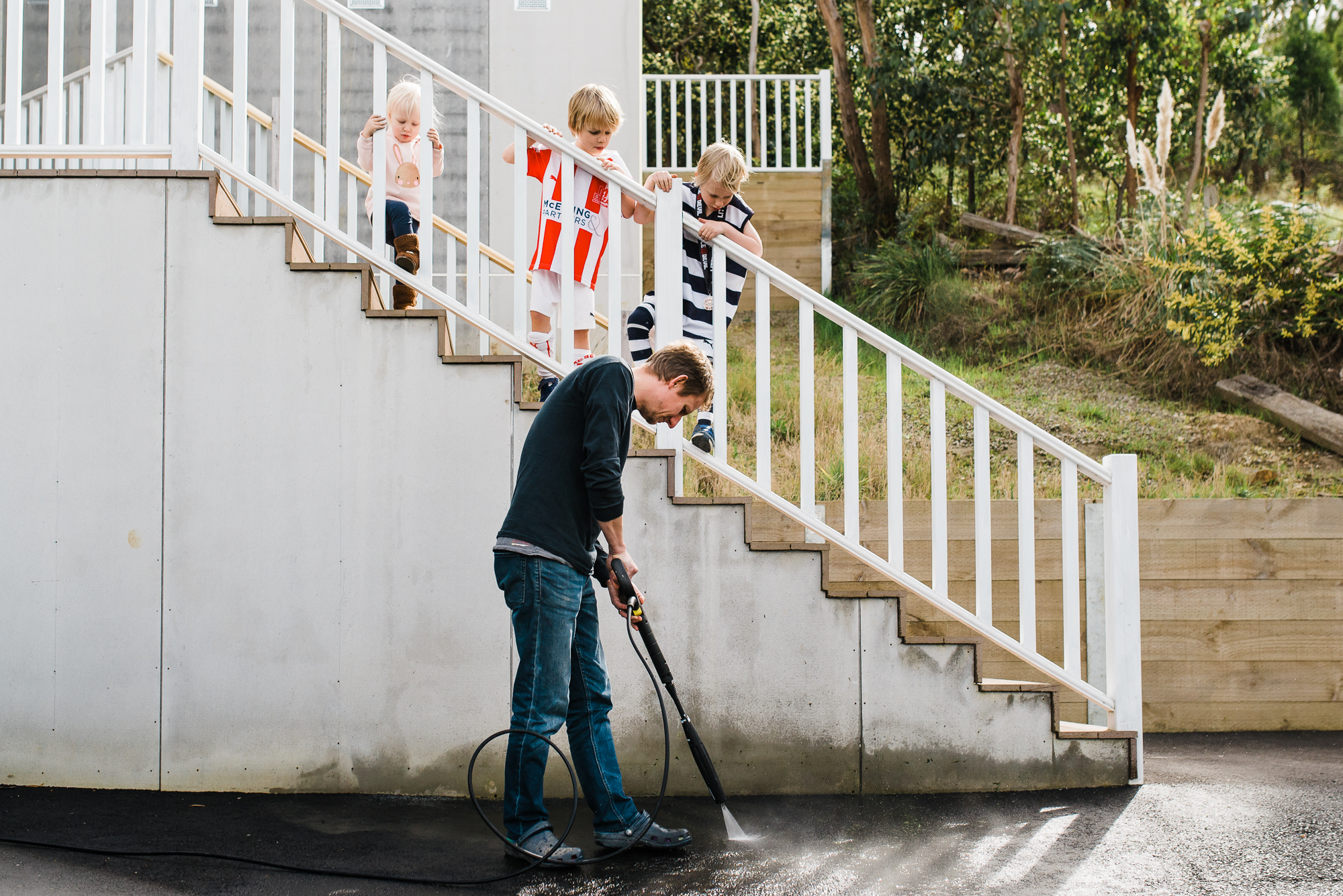 man cleans driveway while children watch on - Documentary Family Photography