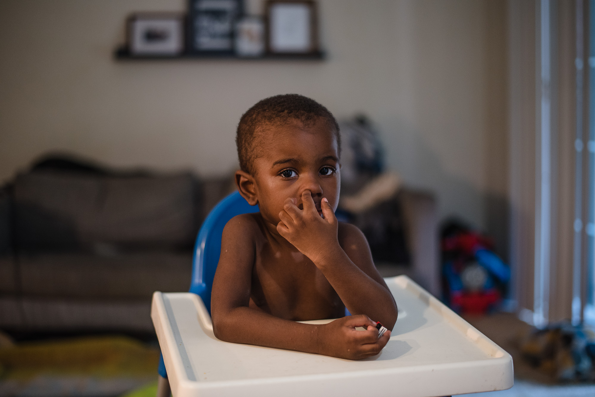 boy in high chair picks nose - Documentary Family Photography