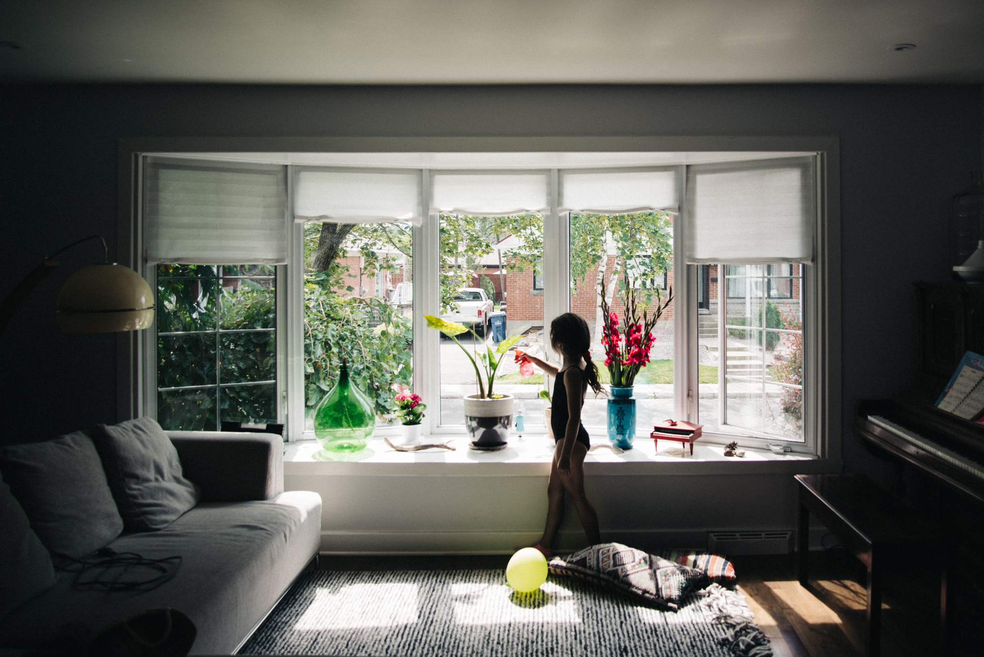 girl sprays plants in window - Documentary Family Photography