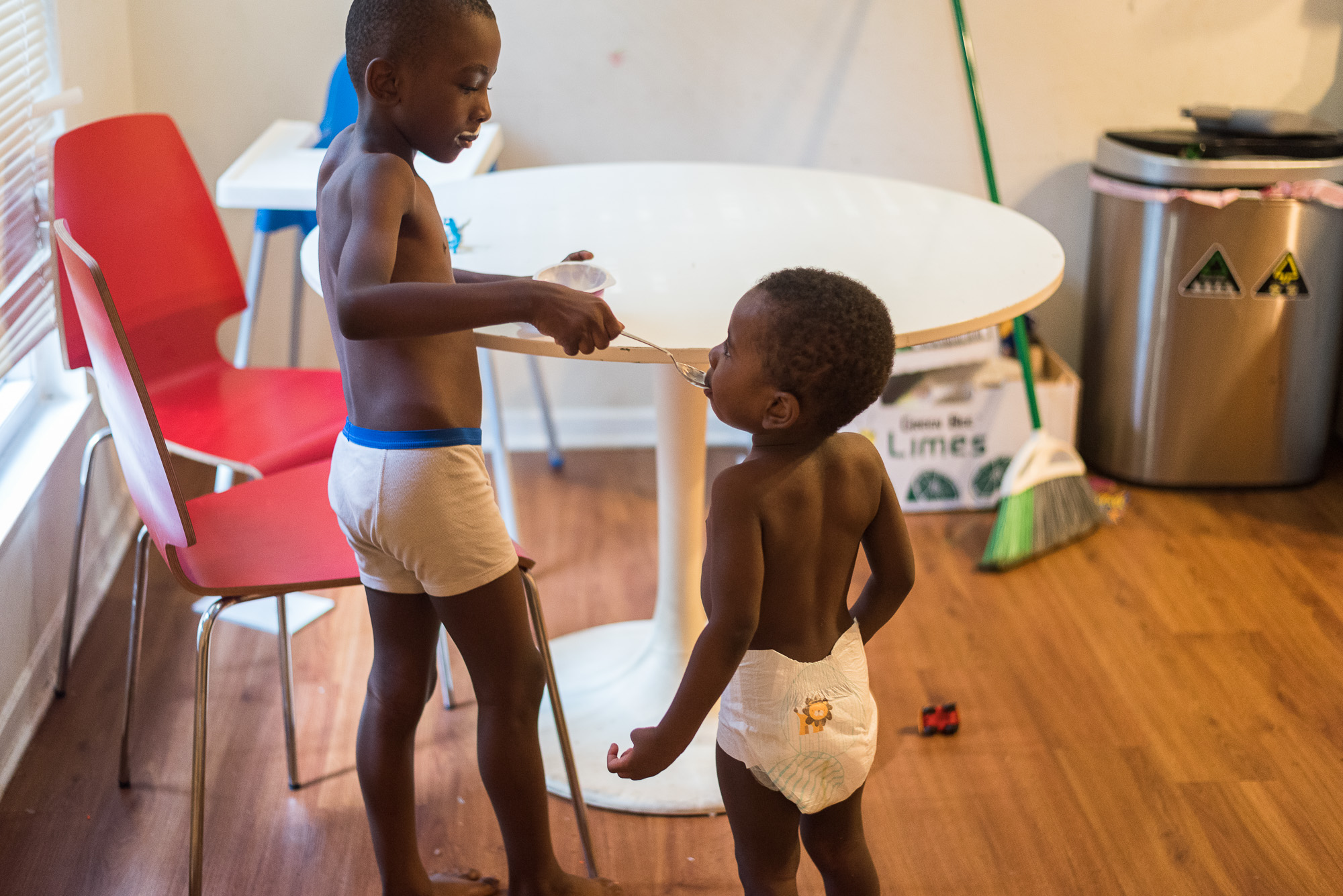 older brother feeds younger at table - Documentary Family Photography