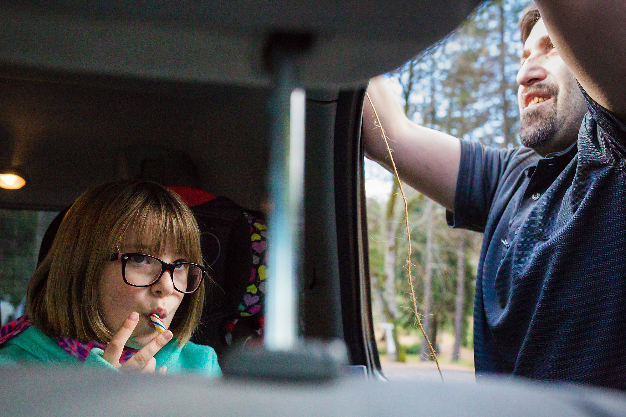 father securing item to roof of car while girl sits in backseat - documentary family photography