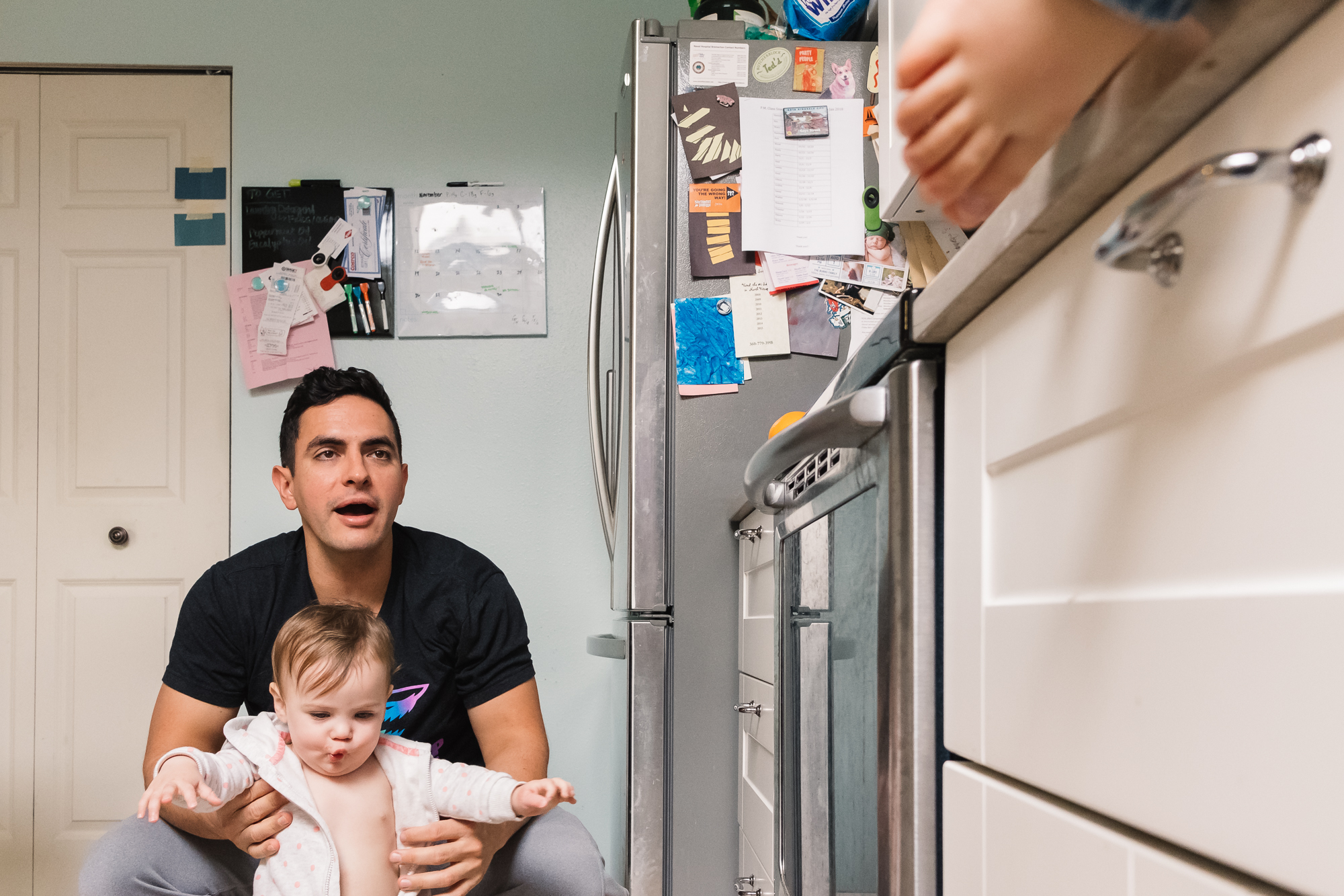 father admonishes kid climbing on counter while tending baby - documentary family photography