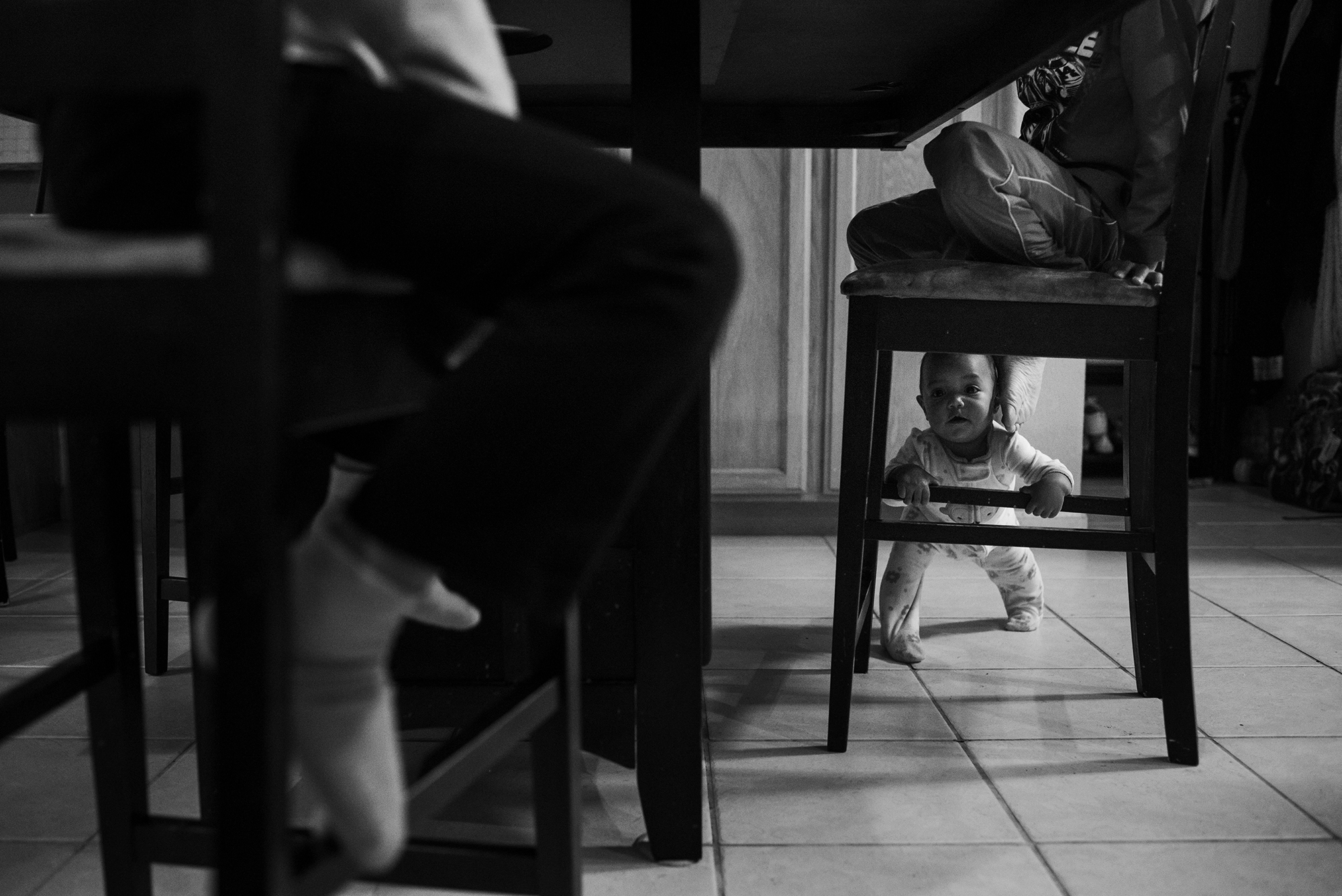 baby peering through chair legs- Documentary Family Photography