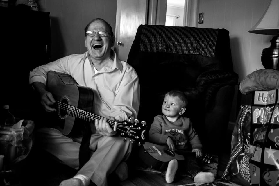 man sings with guitar baby looks on - documentary family photography