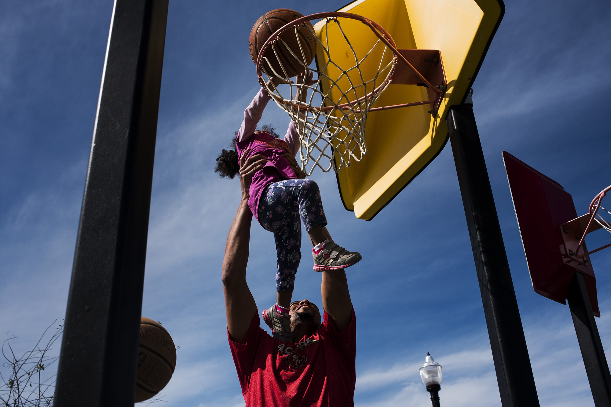 Father lifting child to dunk basketball - documentary family photography