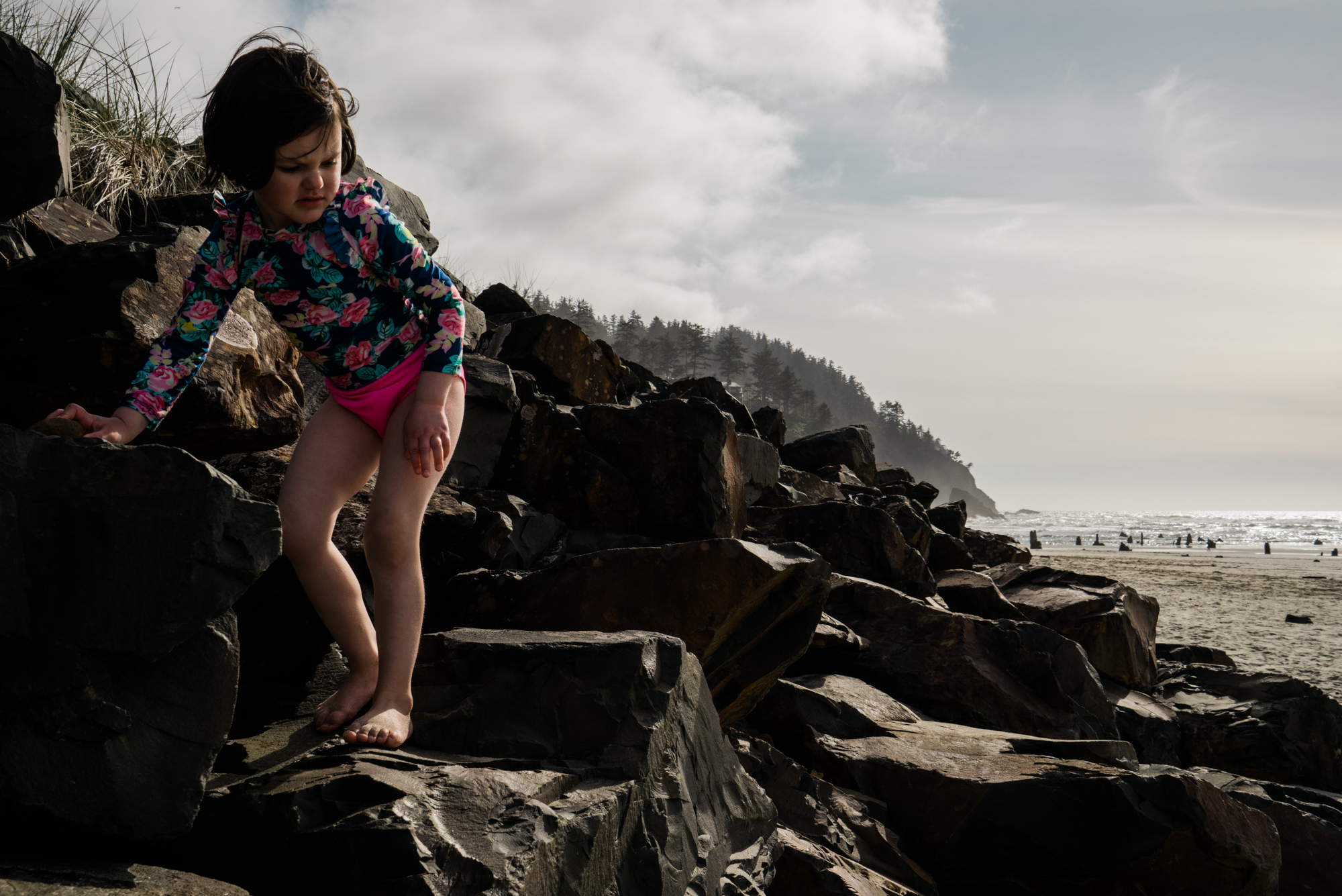 girl climbs on rocks at beach - documentary family photography