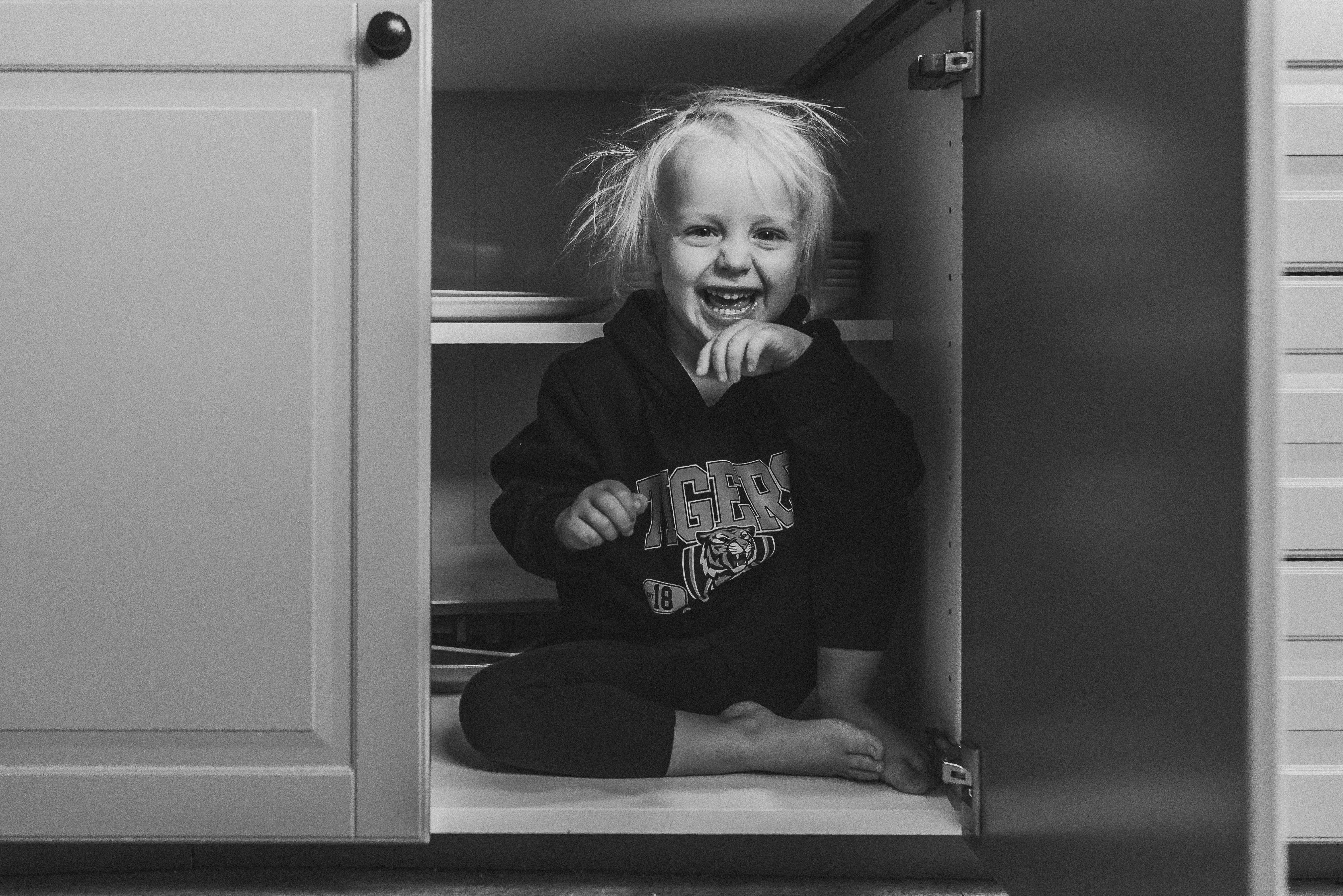 girl hiding in cabinet - documentary family photography