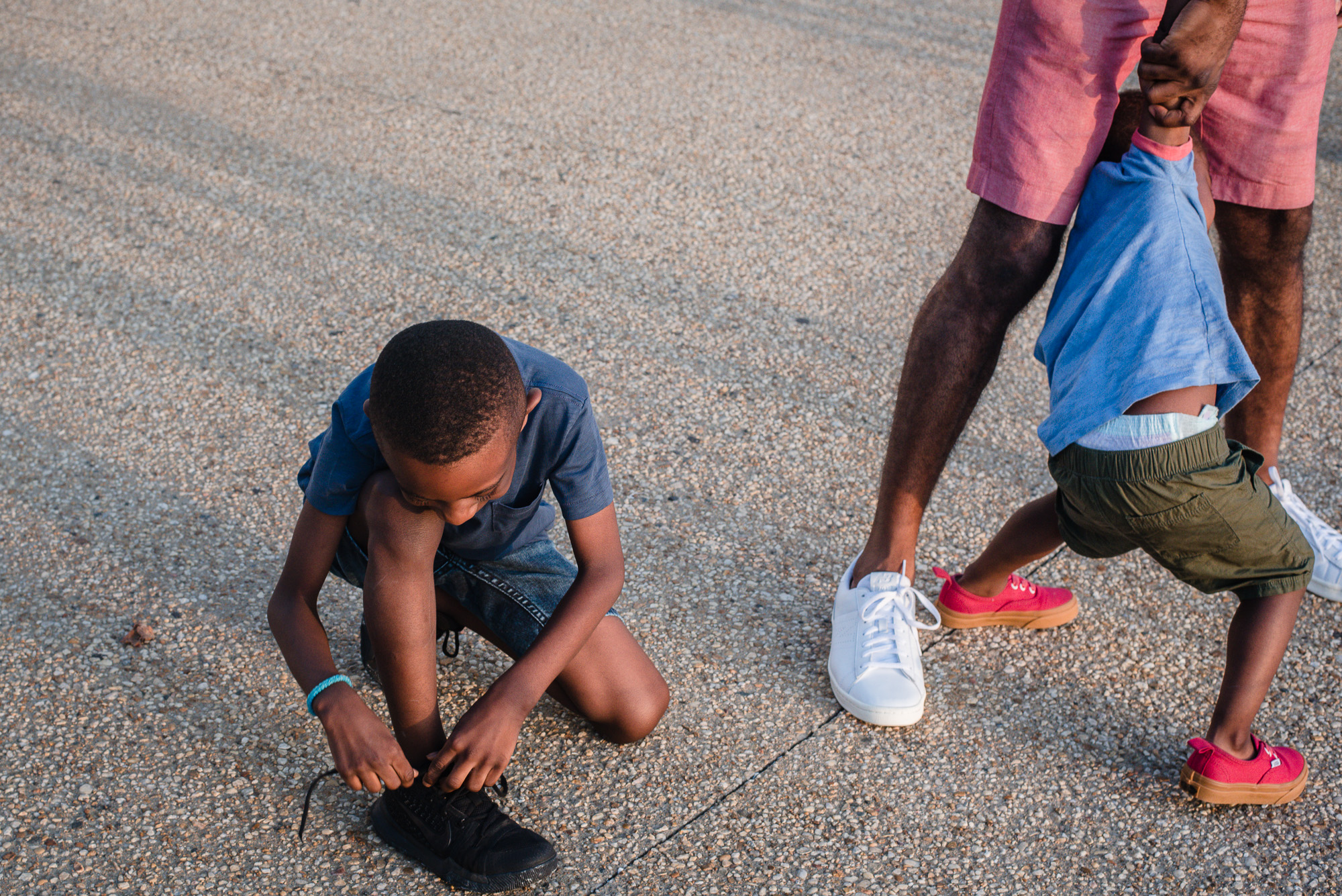 boy ties shoe while brother wrestles with dad - documentary family photography