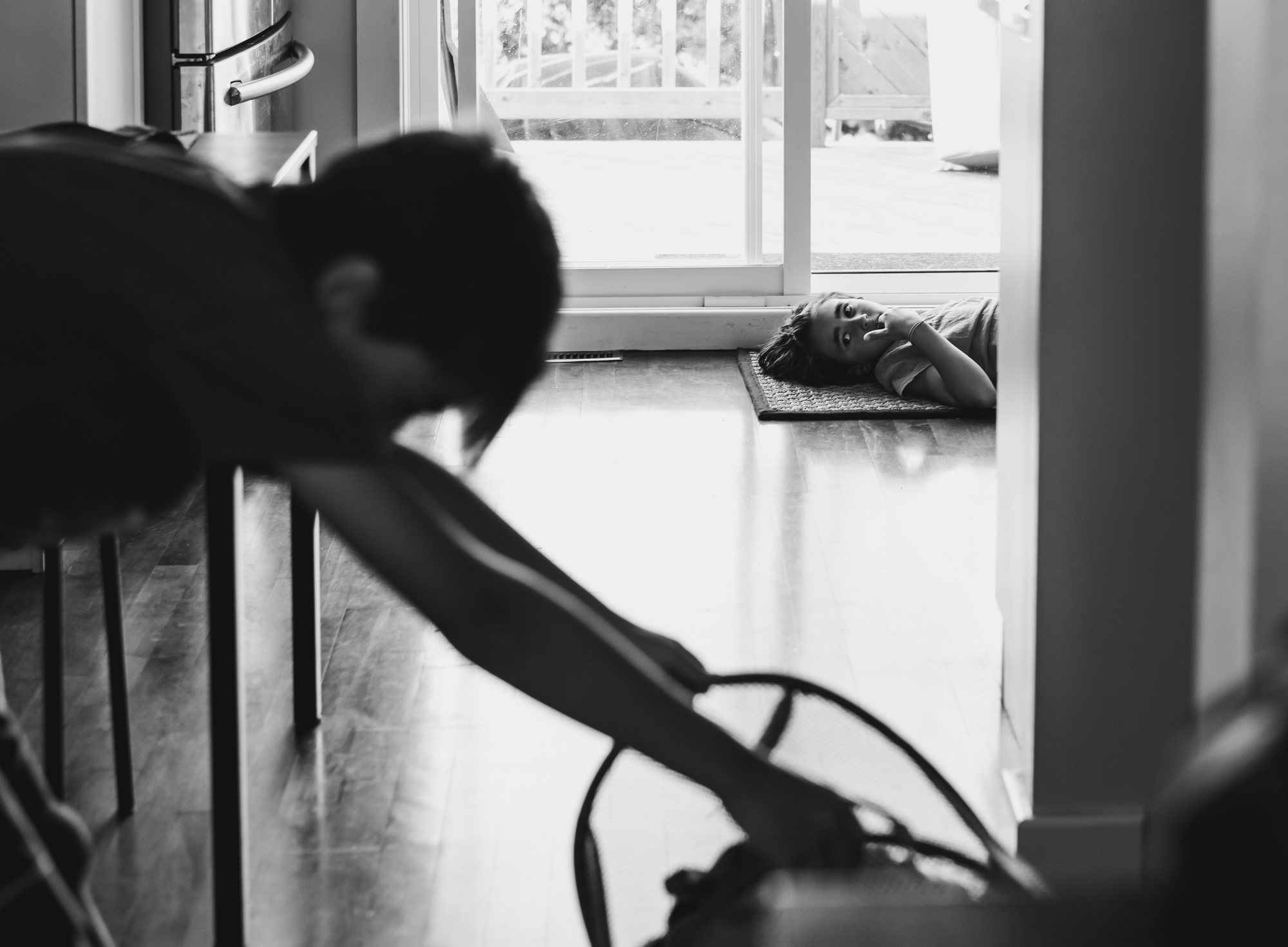 child laying on ground with other child working in foreground - documentary family photography