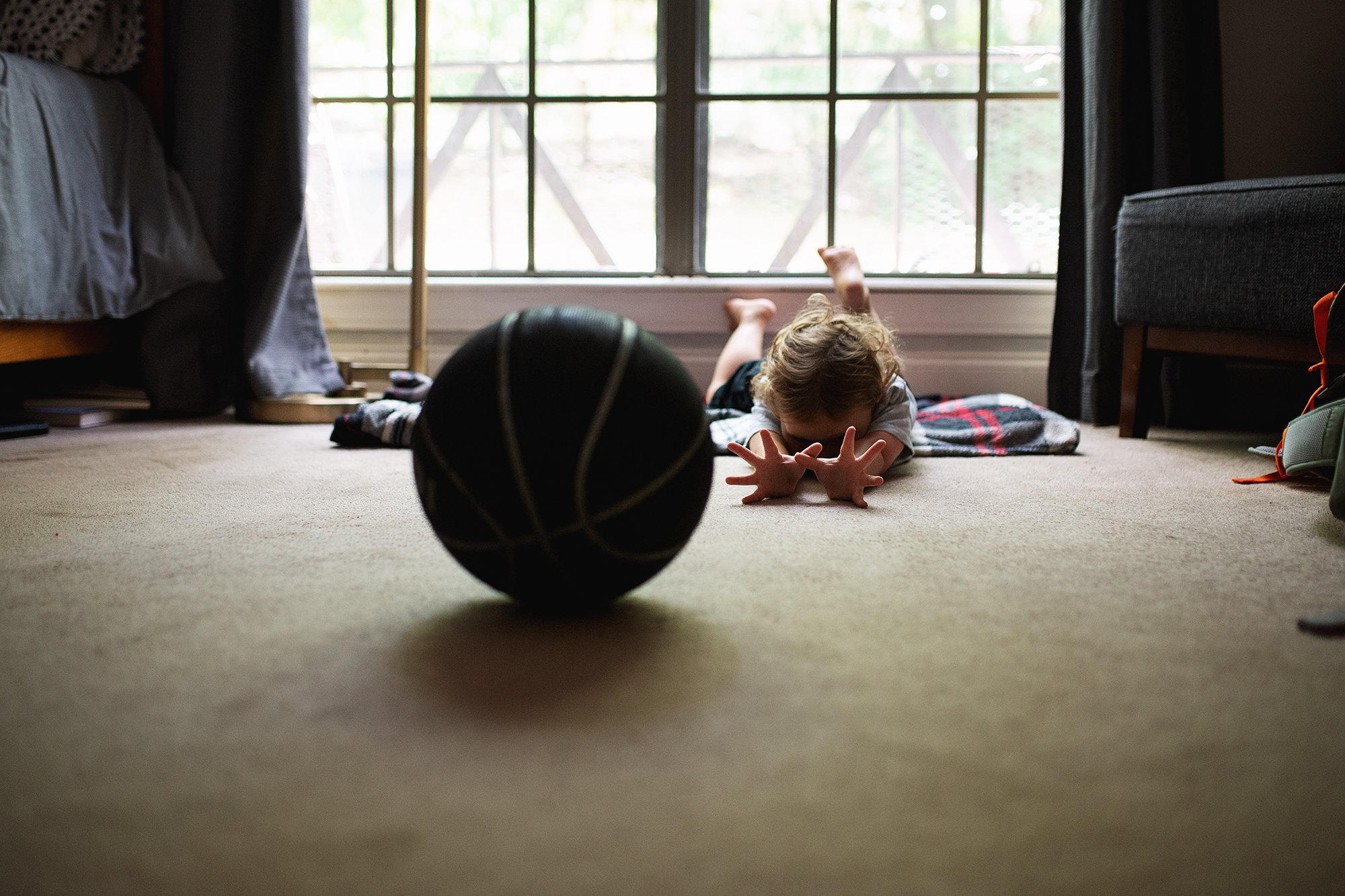 child rolling basket ball along floor - documentary family photography
