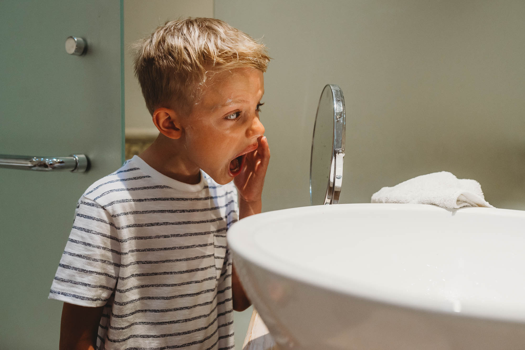 boy examines face in magnification mirror - documentary family photography