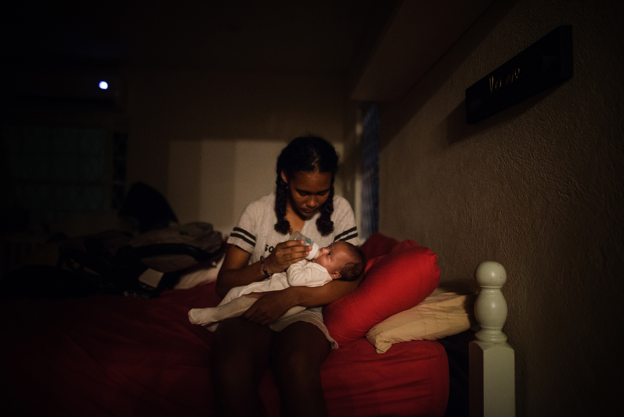 girl feeds baby in dark room - documentary family photography
