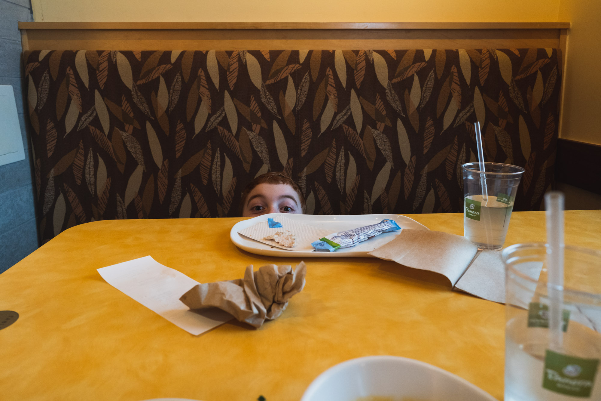 kid peering over restaurant table - documentary family photography