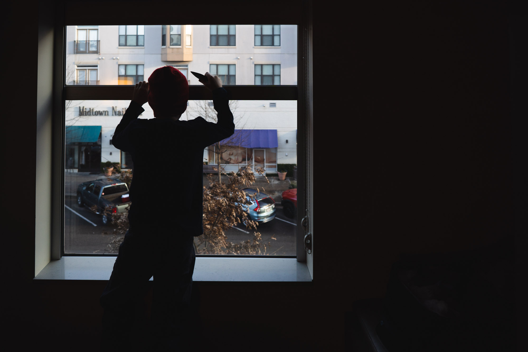 boy looking out window to street below - documentary family photography