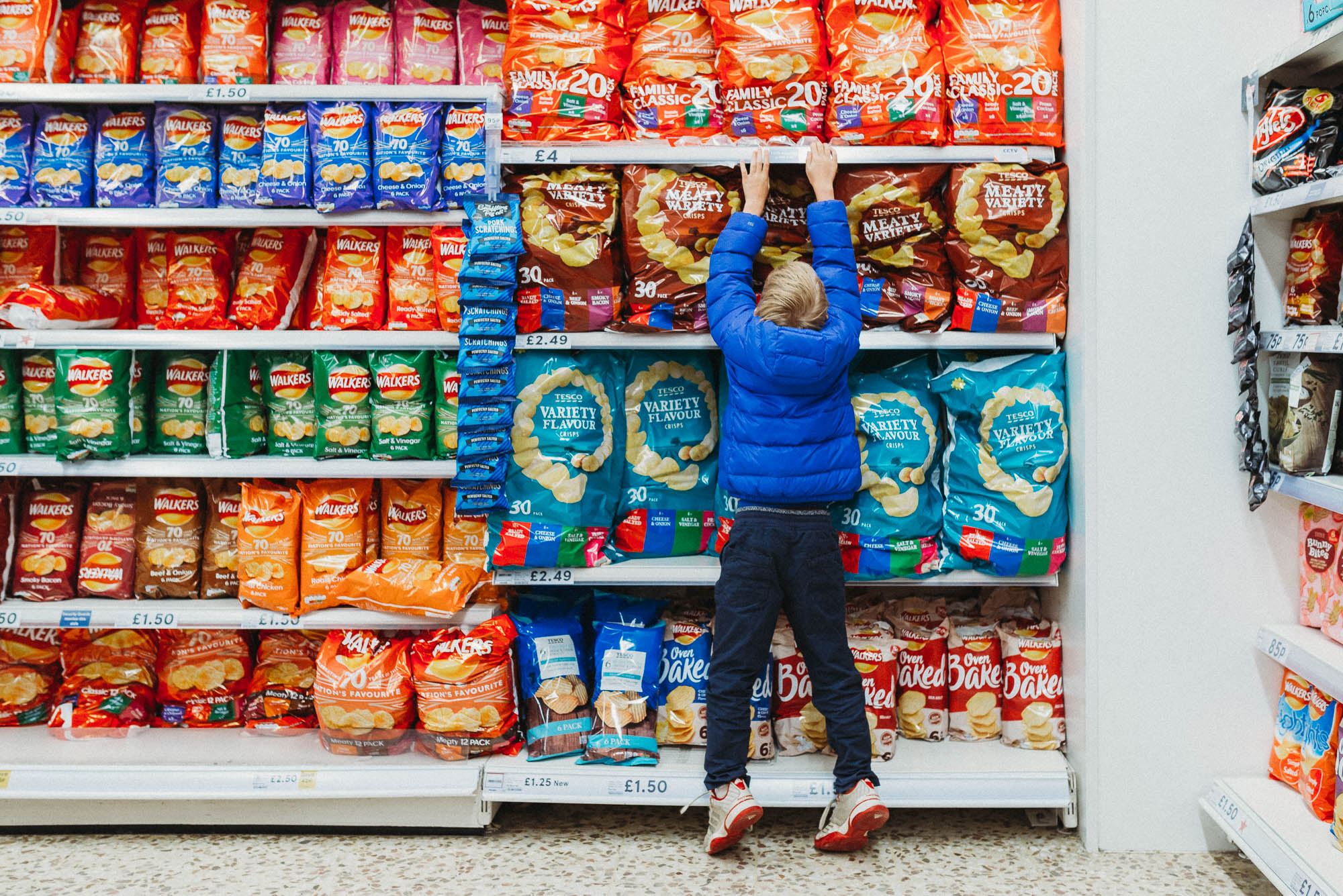 boy pulling on shelf in snack aisle - documentary family photography