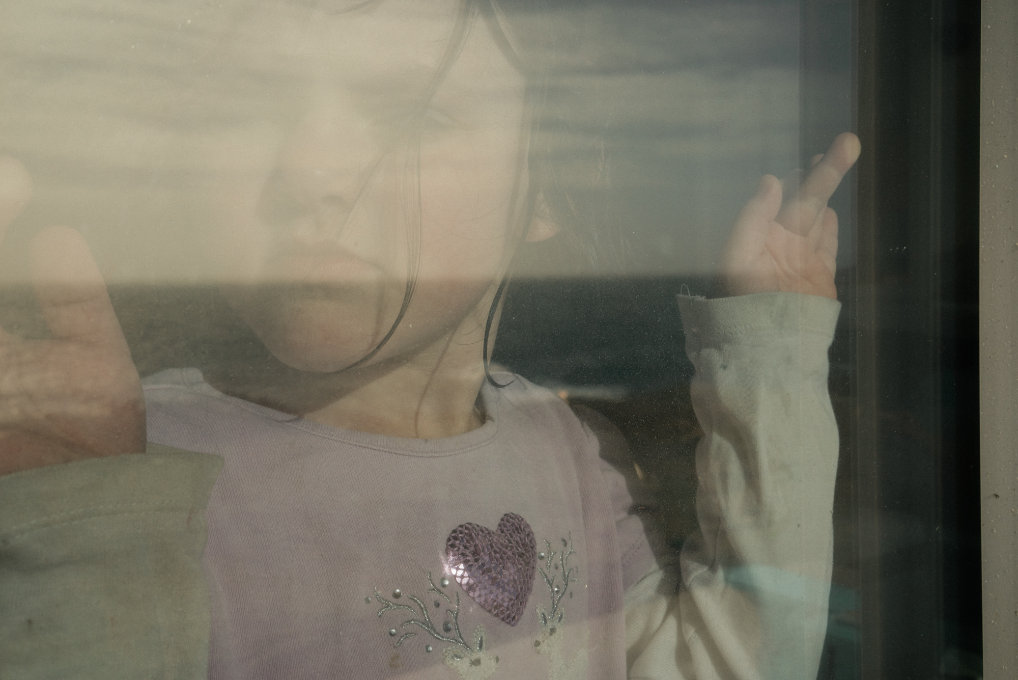girl glaring through window - documentary family photography