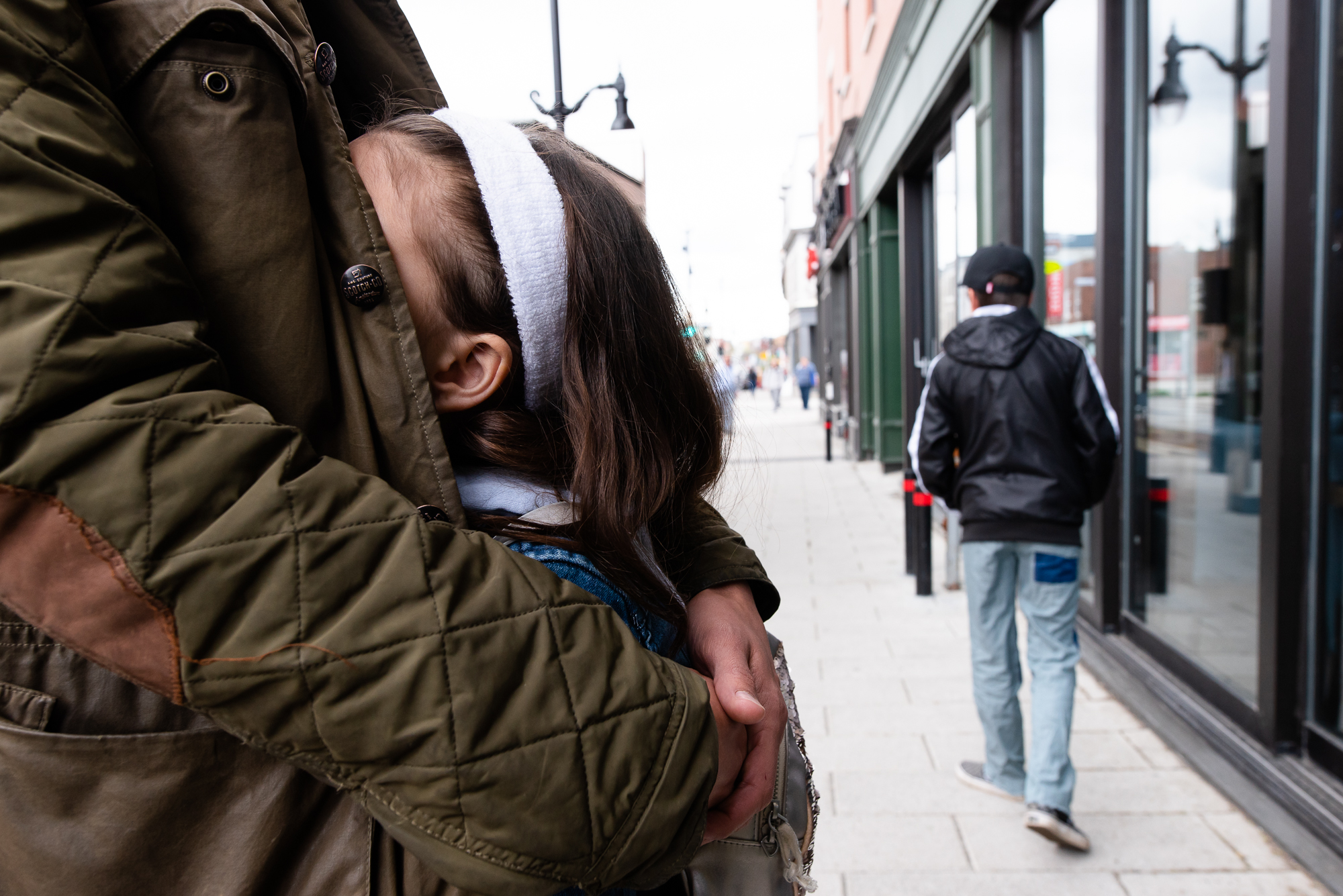 girl hiding in adult's coat - documentary family photography