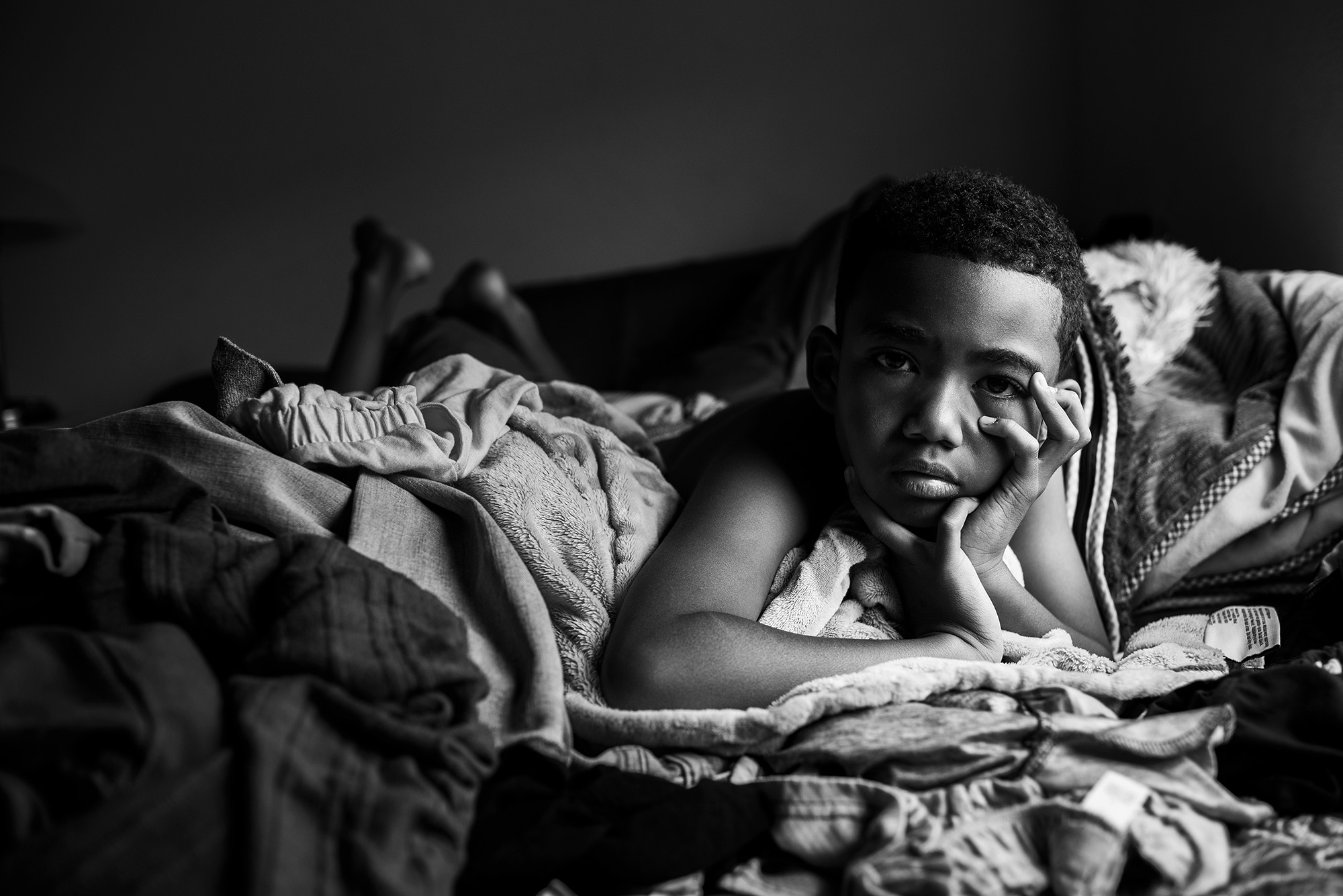 boy wrapped in blankets with head in hands - documentary family photography