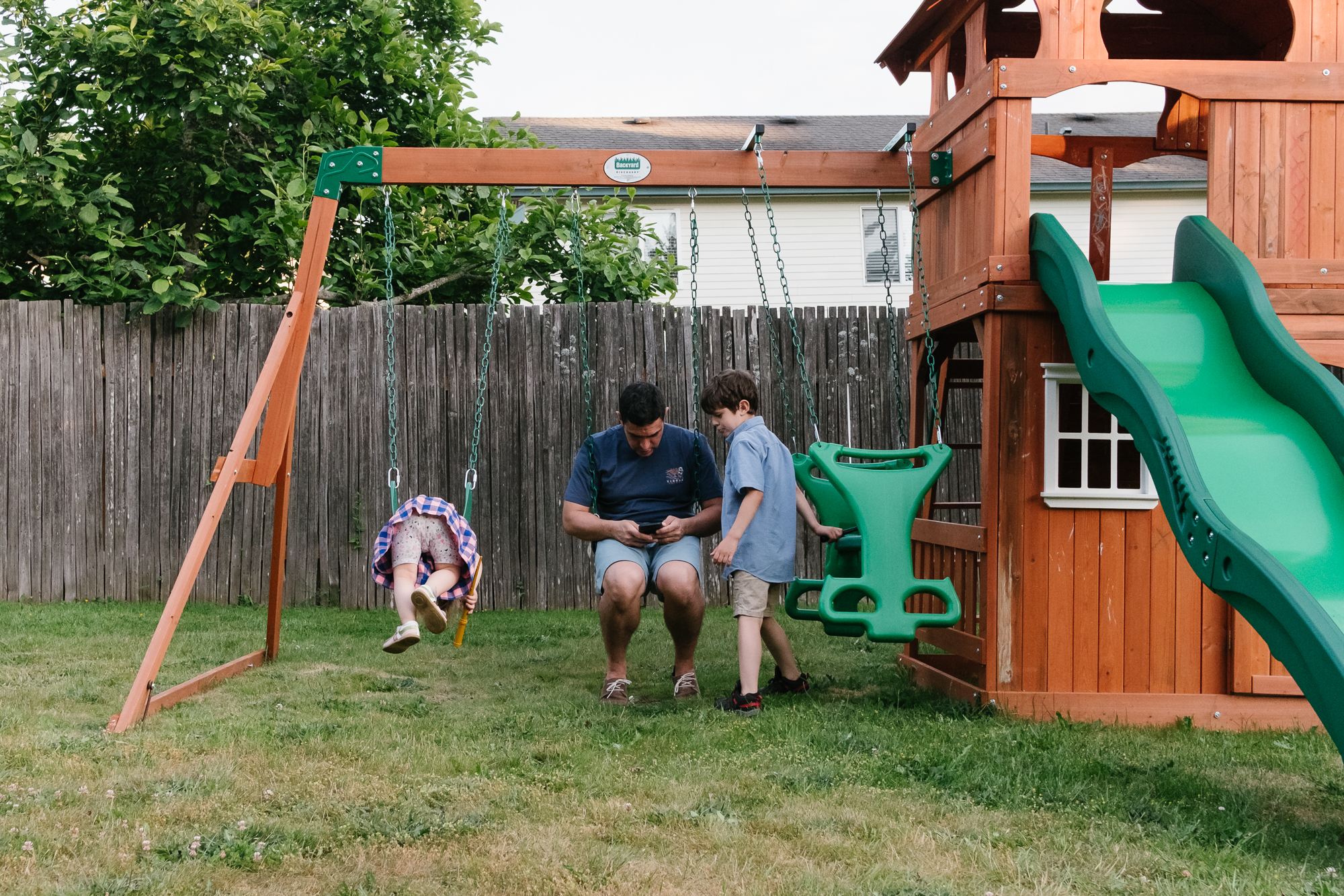 kids on swingset and father with phone -documentary family photography